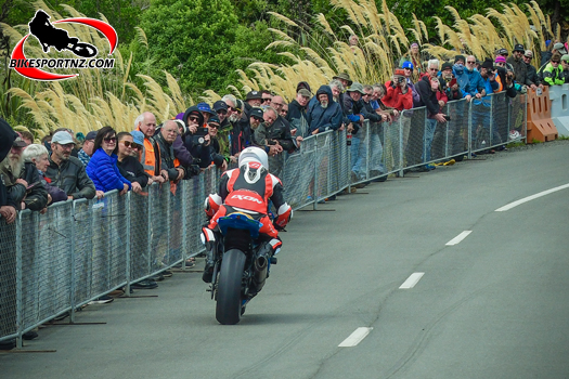The crowd looks on as a competitor blasts out of the start chute and heads up Bluff Hill during the New Zealand Hill Club Championships racing segment of the 2024 Burt Munro Challenge week. Photo by Andy McGechan, BikesportNZ.com